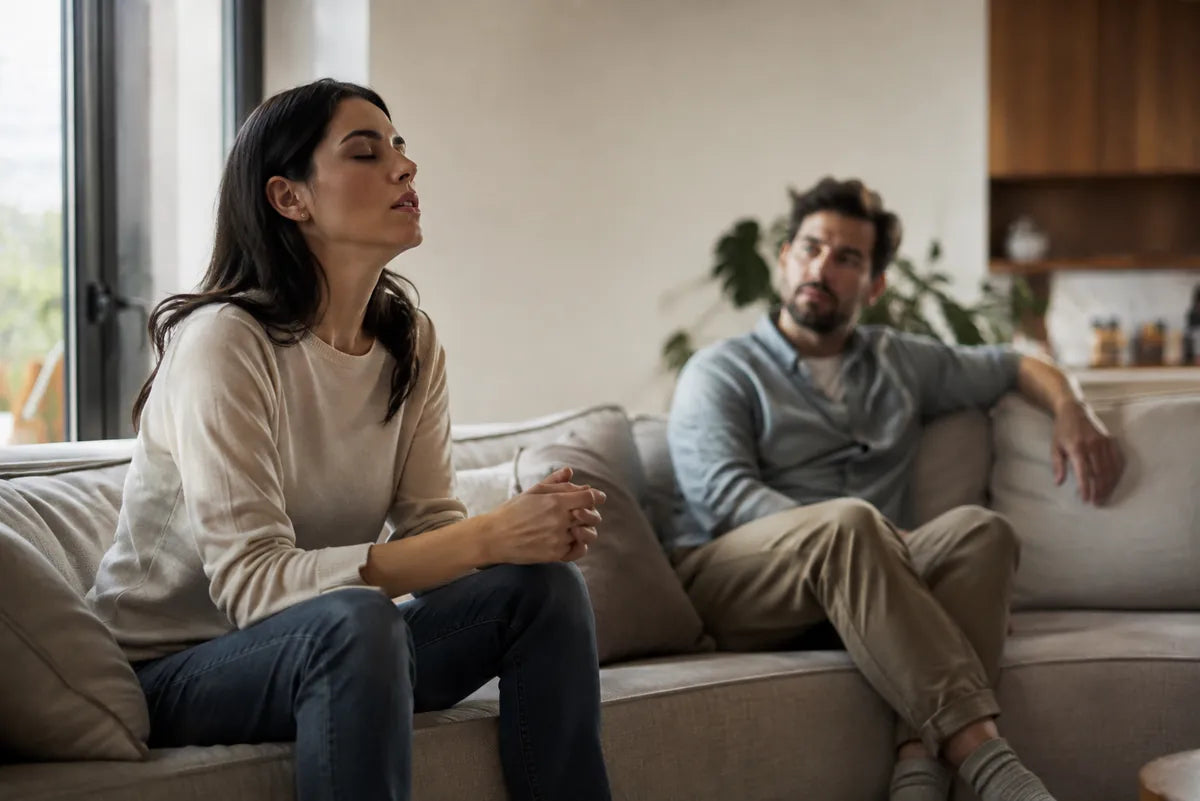 A woman pausing to breathe on a sofa while her partner sits apart after an argument